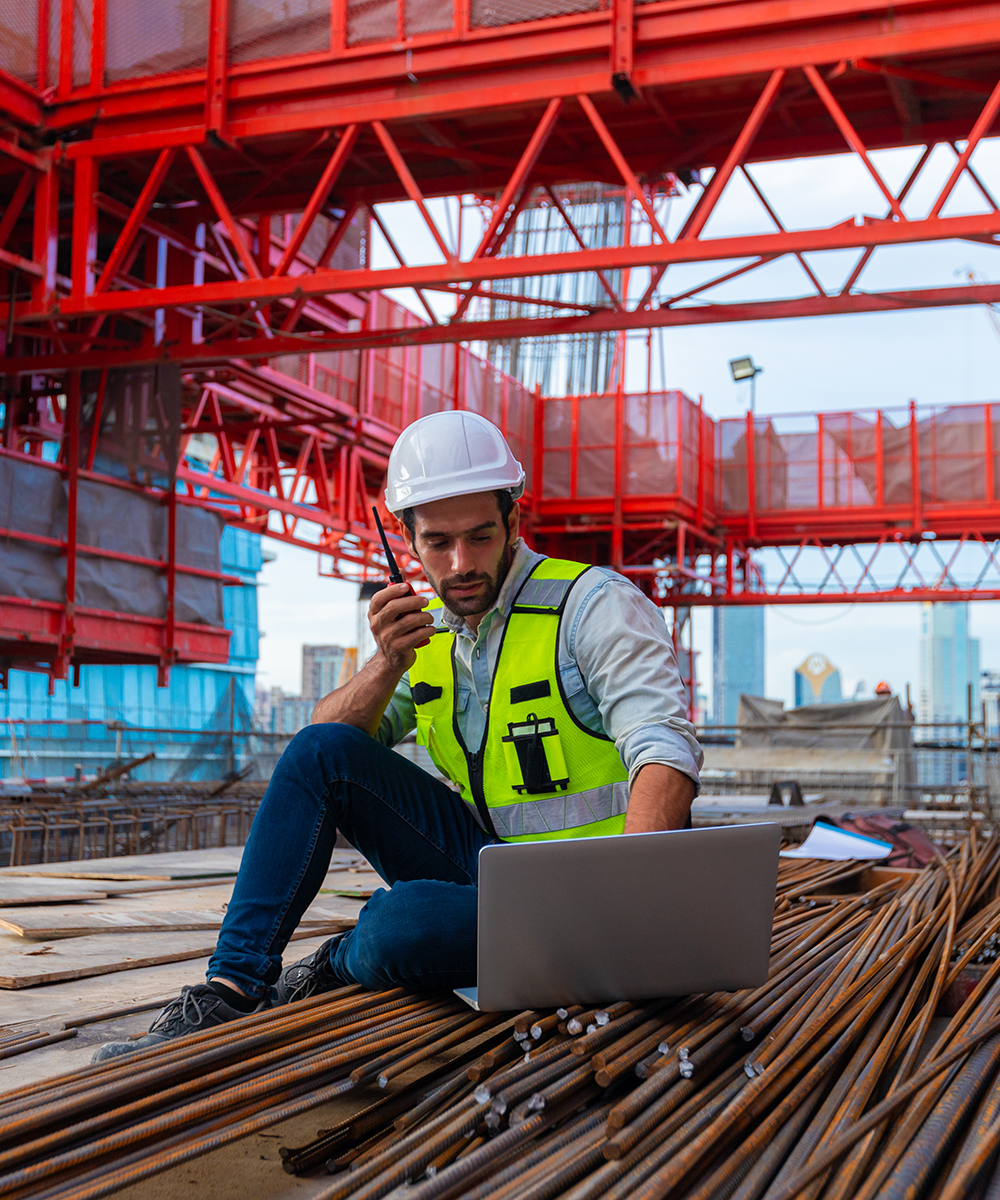 Artigiano impegnato in un cantiere mentre coordina le attività operative con computer portatile e ricetrasmittente. L'immagine rappresenta l'importanza della continuità operativa per professionisti e imprese, dove un fermo macchina può rallentare il lavoro e generare costi. Il noleggio furgoni, Veicoli commerciali e da lavoro a lungo termine aiuta a garantire mobilità, assistenza e veicoli sempre operativi.