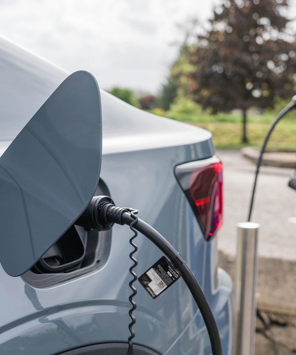 Un'auto elettrica grigia collegata a una stazione di ricarica rappresenta le soluzioni di Noleggio Auto Elettriche, mobilità elettrica e ibrida proposte da RentUp Novara per un noleggio a lungo termine più sostenibile.